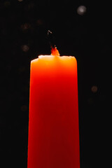 An extinguished orange candle against a dark background in the backlight. Bokeh of glowing dots in...