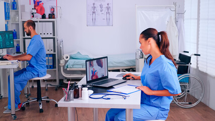 Group of assistents working in hospital office, analysing digital heart presentation and body scan. Medical physician in medicine uniform writing list of consulted, diagnosed patients, making research