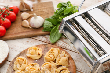 Raw pasta with machine on wooden background