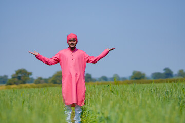 Young indian farmer standing his wheat field and giving happy expression