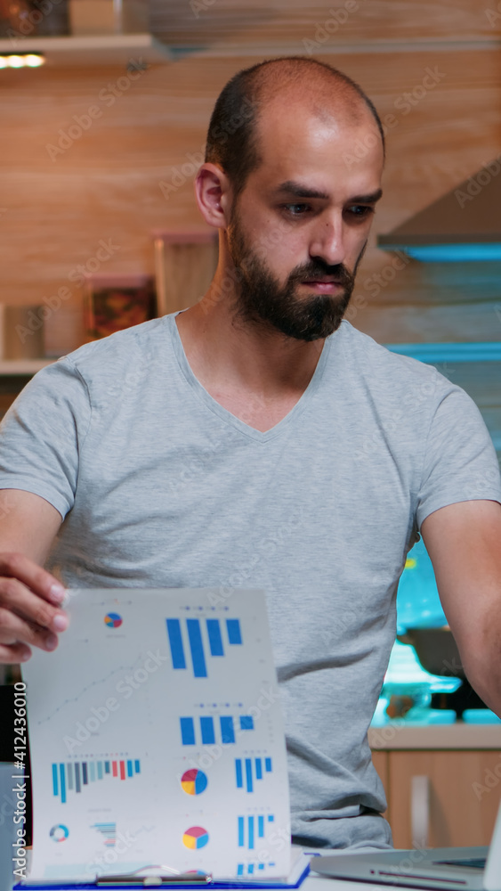 Poster focused busy entrepreneur checking graphics from clipboard using laptop looking on laptop working fr