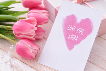 Beautiful flowers, gift and greeting card for Mother's Day on light wooden background