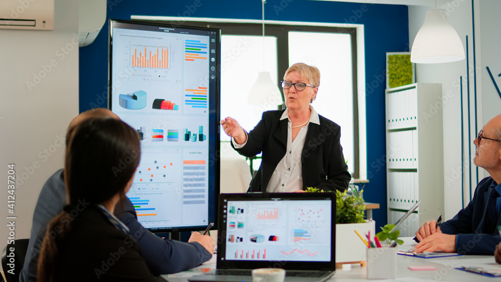 Aufkleber elderly project manager pointing at desktop presenting statistical data, briefing diverse group of e