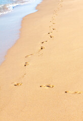 Fototapeta na wymiar A path made of footprints of bare human feet goes along the yellow sand of the coast along the sea