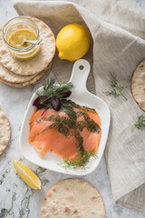 Gravlax Graved Lachs, ein roh gebeizter Fisch mit Dill auf Platte mit Hovmästarsås Senf Soße, Knäckebrot, Zitrone und Leinen Tuch auf hell Marmor Hintergrund
