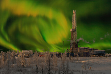 The rig and the northern landscape of the oil and gas field against the polar lights. Landscape with beautiful night sky in winter in the Arctic