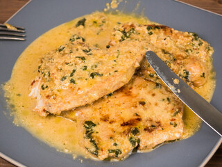 Fried turkey breast steaks with creamy sauce on a large plate with fork and knife on a wooden table, close-up