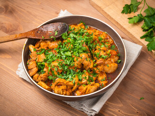 Chicken curry sprinkled with chopped parsley in a bowl on a wooden brown table with a kitchen board