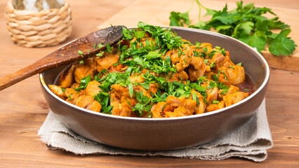 Chicken curry sprinkled with chopped parsley in a bowl on a wooden brown table with a kitchen board