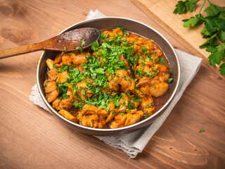 Chicken curry sprinkled with chopped parsley in a bowl on a wooden brown table with a kitchen board