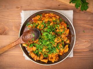 Chicken curry sprinkled with chopped parsley in a bowl on a wooden brown table, top view