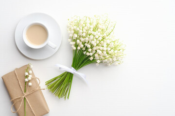 Coffee mug with bouquet of flowers lily of the valley and gift box on white background. Flat lay,...