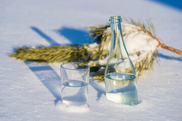 Glass bottle and glass of water on a white snow in winter
