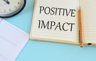 Positive Impact text written in notebook, light blue background, business concept