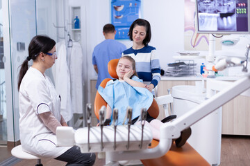 Little girl in pediatric dentist office touching face with painful expression because of tooth...