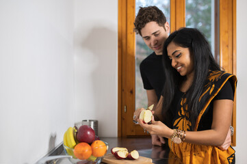 Multi-ethnic couple at home cutting fruit in the kitchen. Indian woman with traditional dress and...