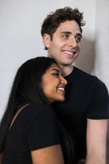 Obraz premium smiling multiethnic young couple with black clothes looking out the window hugging each other.
