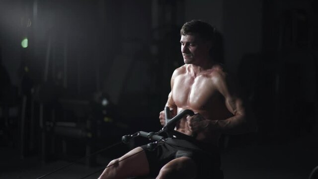 Athletic man in the Gym lifting blocks on rowing machine, training on block device and gym equipment, night training, cinematic light.