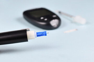Close up of needle of lancing device for diabetes treatment with blood glucose sugar meter and syringe in blurry background
