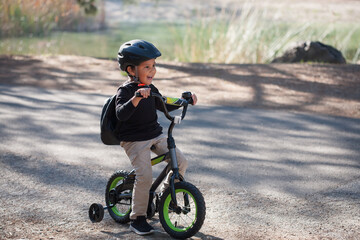A five year old boy learning to ride a bicycle with training wheels, and a lake in the background.