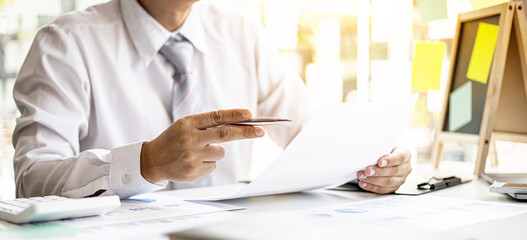 A businessman pointing at a document with a pen to check the financial numbers, he is sitting in...