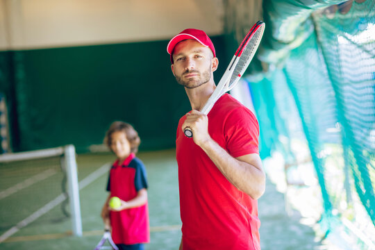 Young bearded man in a red cap standing with a tennis racket