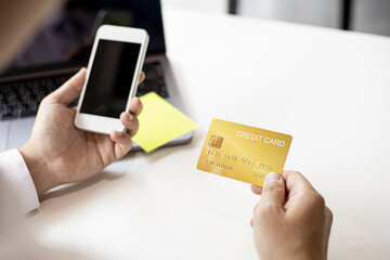 A man with a yellow credit card and a smartphone is filling out his credit card information in order to pay for online purchases ordered from online shopping sites. Concept of using a credit card.