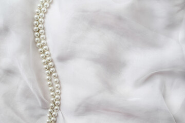 A necklace of pearls lies on a white cloth

