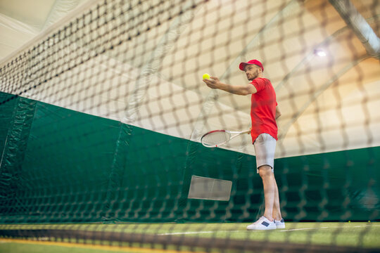 Young bearded man in a red cap ready to hit the tennis ball