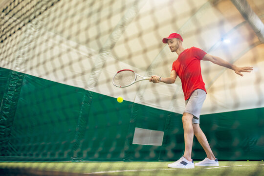 Young bearded man in a red cap ready to hit the tennis ball