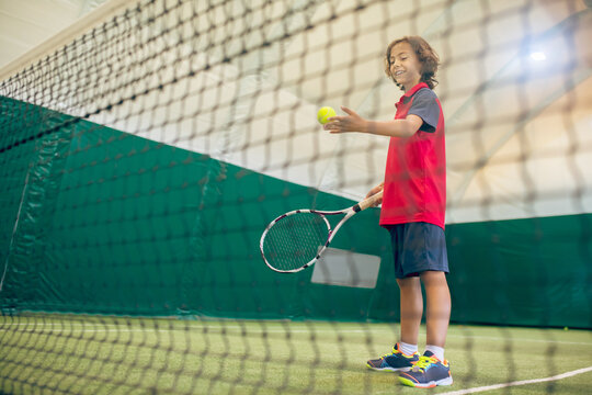 Dark-haired boy in red tshirt ready to hit the tennis ball