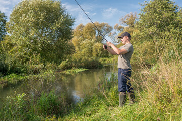 Fisherman holding a fishing rod by the river. Summer sunny day