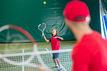 Waist up picture of a man in red cap playing tennis with a boy