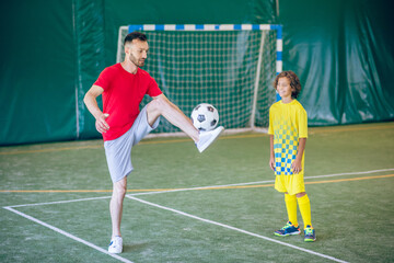 Obraz premium Man in a red tshirt kicking a ball, a boy watching him