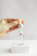 Glass jar for natural cosmetics on a white background on a white podium with a flower inside with a female hand. Trendy minimalistic abstract collection. The beauty of a woman. Natural background.