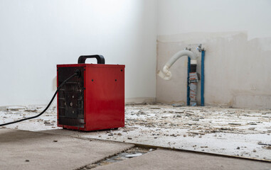 red fan heater at a construction site, remnants of tile adhesive and drain pipes in the background