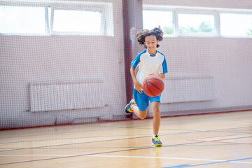 Boy in sportswear running after the ball in a gym