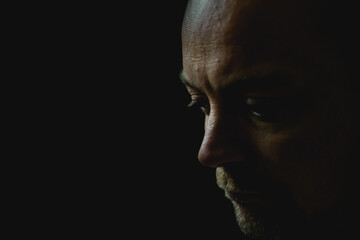 Portrait of an adult white man looking sad or worried. Isolated on a black background in low light. Shallow depth of field. High quality photo