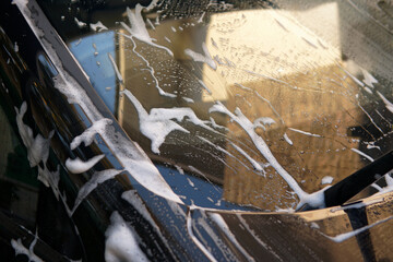 Closeup white soap and suds on windshield with reflect of roof house outdoor at evening. Carwash...