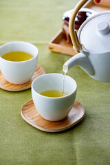 Cups of green tea and teapot.
Pouring fresh green tea in the cups.