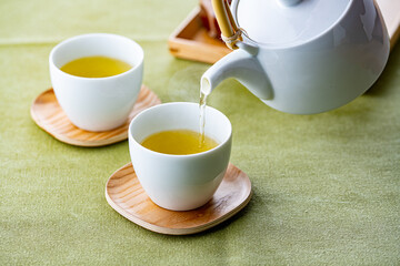 Cups of green tea and teapot.
Pouring fresh green tea in the cups.
