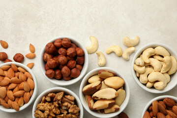Bowls with different nuts on white textured background, top view