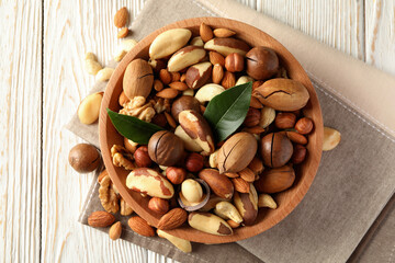 Bowl with different tasty nuts on white wooden background