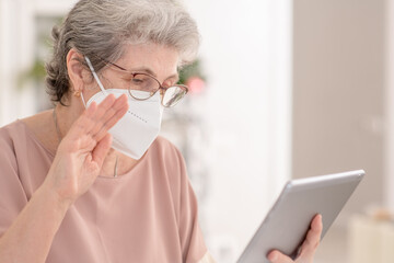 Senior woman wearing protective face mask talks with his family on video call during the coronavirus epidemic