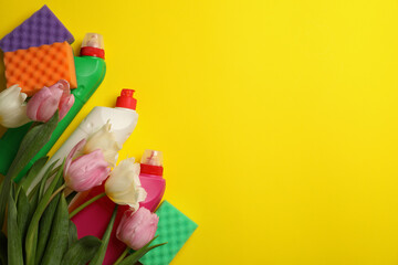 Detergents, sponges and tulips on yellow background