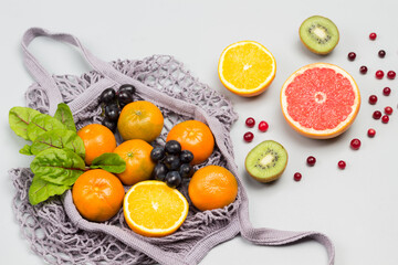 Reusable mesh bag with fruits. Tangerines, grapefruit, kiwi, grapes and chard leaves on table