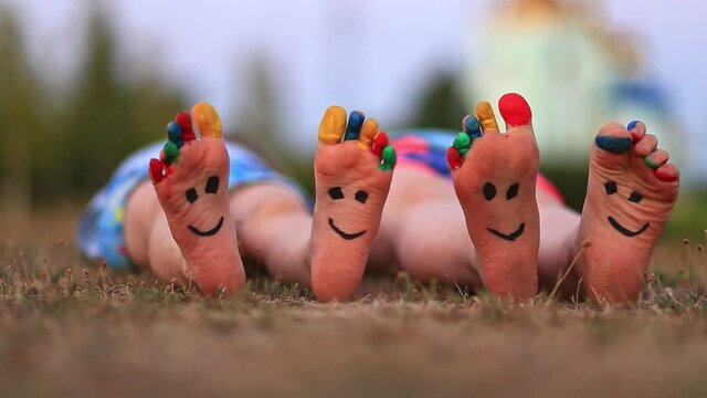 Two little child have fun lying outdoor on grass. Feet of child with painted smile faces.