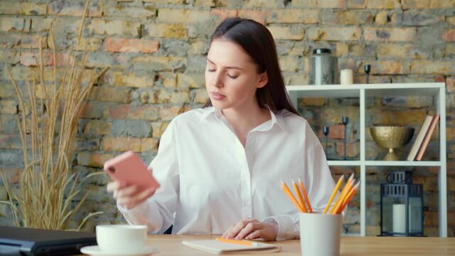 Young beautiful woman making notes at tha table and talking on the phone