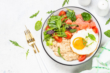 Savory breakfast. Oatmeal porrige with salted salmon, egg and fresh salad. Healthy food, balanced nutrition. Top view on white table.