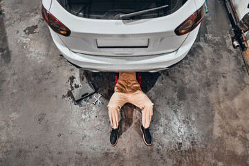 Mechanic lying and working under car at the repair garage.